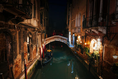 Illuminated bridge over canal amidst buildings in city at night