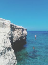 Men jumping in sea against clear blue sky