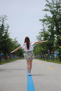 Full length rear view of woman with arms outstretched walking on street blue line