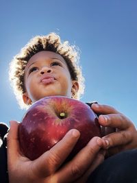 Portrait of boy holding apple against sky