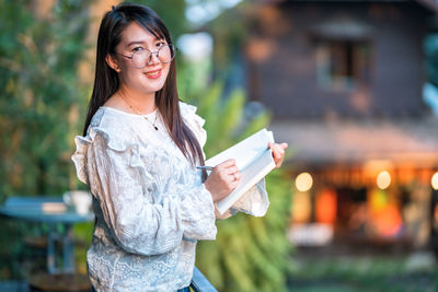Portrait of smiling young woman holding smart phone in city