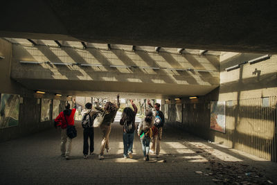 Multiracial young friends with hands raised walking together through underpass