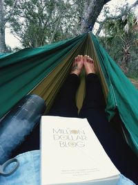 Low section of woman with book relaxing in hammock