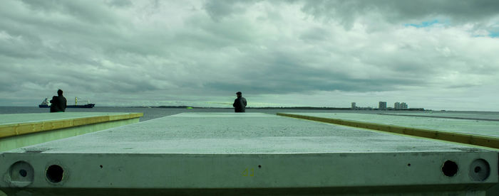 Rear view of people looking at sea against cloudy sky