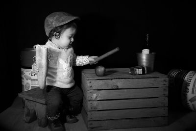 Cute boy holding bread and rolling pin by table against wall