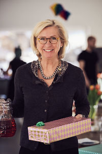 Portrait of smiling senior woman holding gift box and juice while standing at home