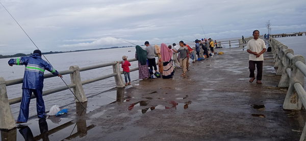 Rear view of people walking on sea shore against sky