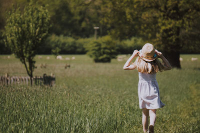 Rear view of girl walking on grassy field against trees
