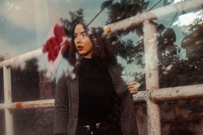 Young woman standing by metallic railing seen from glass