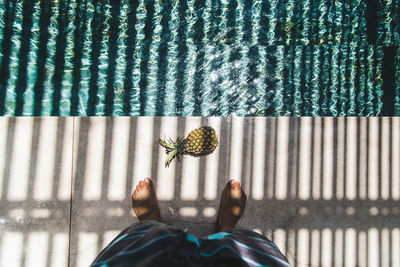 Low section of person standing by pineapple and swimming pool