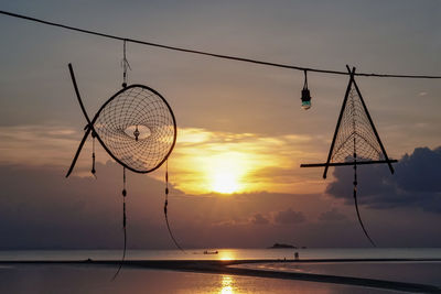 Silhouette dreamcatchers hanging at beach against cloudy sky