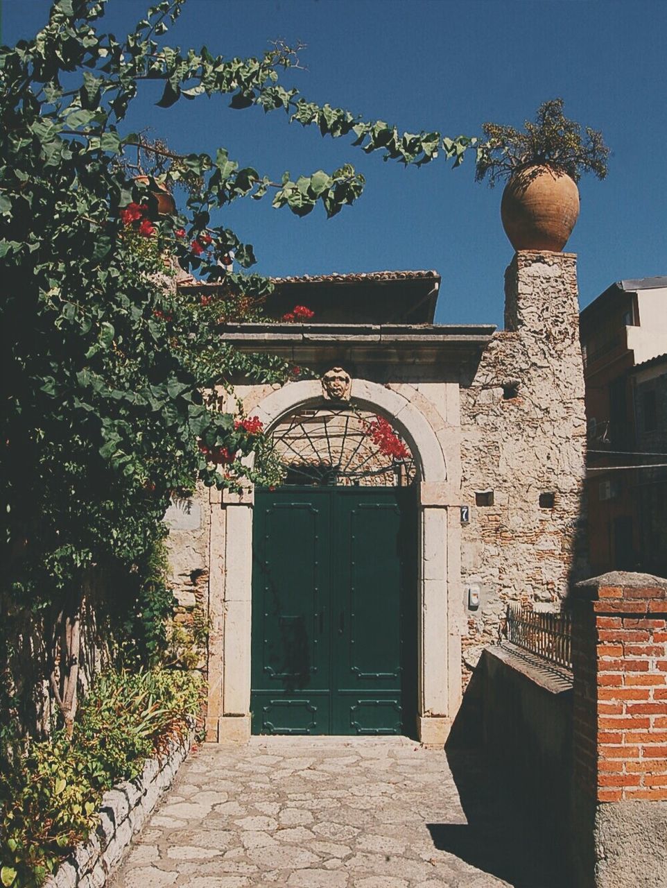 architecture, building exterior, built structure, low angle view, lantern, clear sky, house, blue, lighting equipment, entrance, decoration, tree, hanging, plant, wall - building feature, street light, outdoors, religion, potted plant, no people