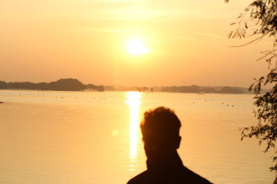 Silhouette man in sea against sky during sunset