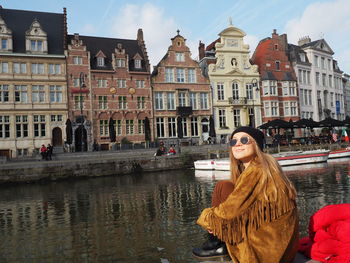 Woman with buildings against sky in canal