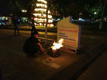 Man sitting by illuminated fire on street at night