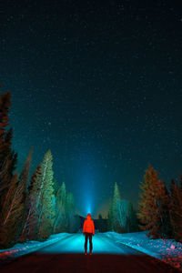 Full length rear view of woman walking on street against sky at night