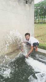 Young man spraying water by wall at pond