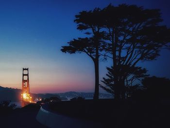 Silhouette trees by road against sky at sunset