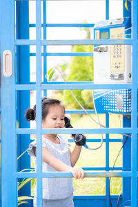 Cute girl talking on phone while standing in blue telephone booth