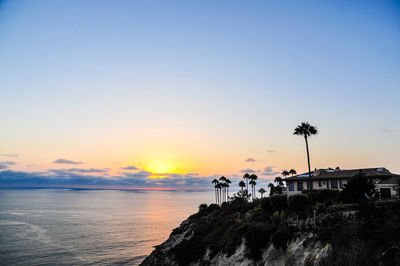 House on cliff by sea against sky during sunset