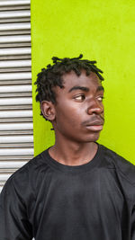 Portrait of young man looking away against green wall