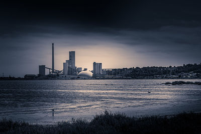 City by river against sky during sunset