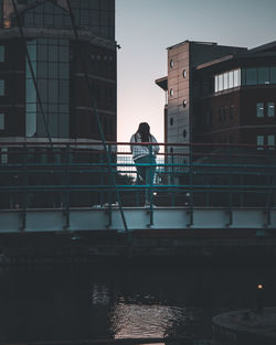 Rear view of man standing by railing against buildings in city