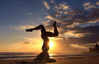 Side view of woman performing headstand on beach at sunset