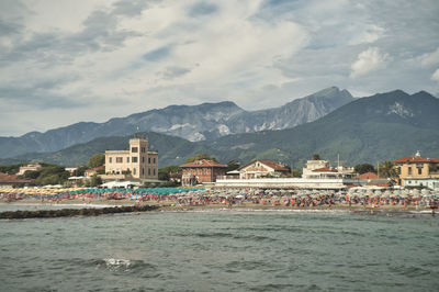 Buildings at waterfront against cloudy sky