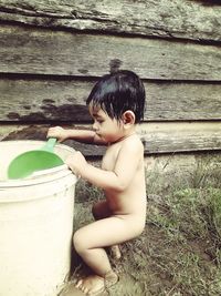 Side view of shirtless boy standing on wood