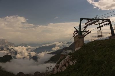 Low angle view of ski lift on mountain against sky in foggy weather during sunset