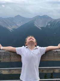 Boy with arms outstretched standing against mountains