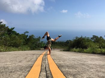 Rear view of woman jumping on road against sky