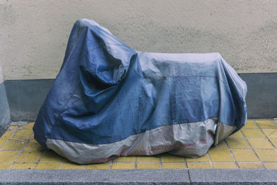 Motor scooter covered with tarpaulin on footpath by wall