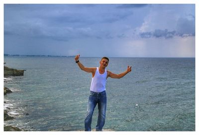 Portrait of man standing with arms outstretched against sea