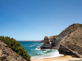 Scenic view of rocky beach against clear blue sky