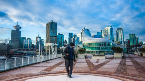 Front view of man walking on footpath against city against sky