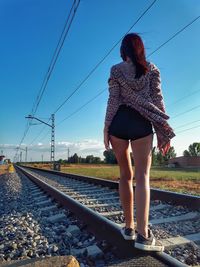 Rear view of woman standing on railroad track against clear sky