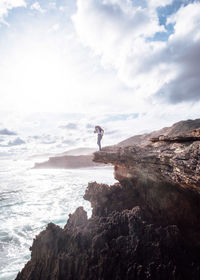 Man on cliff by sea against sky