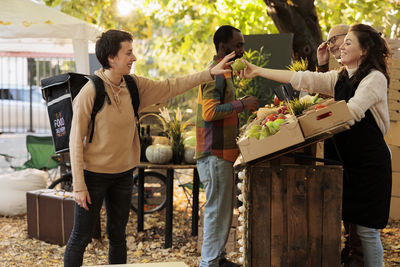 Portrait of smiling friends using digital tablet while standing in park