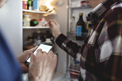 Senior woman holding smart phone standing by retired man in kitchen at home