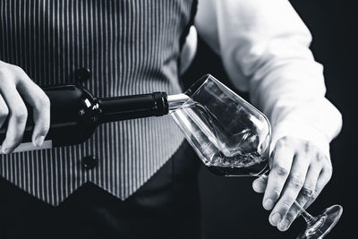 Midsection of bartendar pouring wine in glass