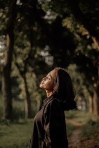 Side view of young woman standing against trees