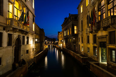 Canal amidst illuminated buildings in city at night