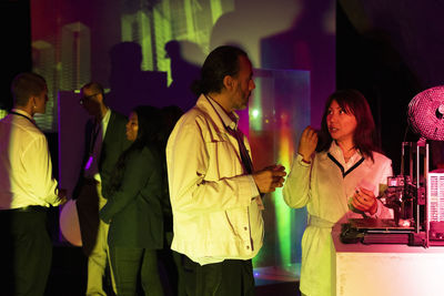 Businesswoman discussing strategy with male colleague by 3d printer in illuminated workshop