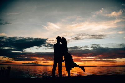 Silhouette couple standing by sea against sky during sunset