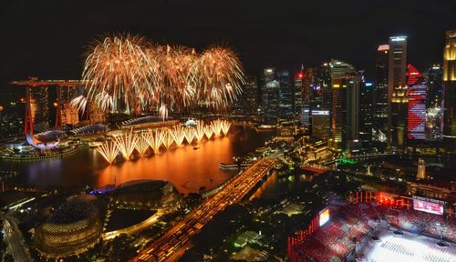 High angle view of illuminated modern buildings by river at night with fireworks