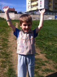Smiling boy with arms raised standing on land during sunny day