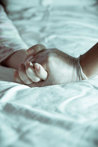 Cropped image of doctor holding patient hand on bed