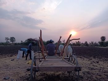 Man sitting on field against sky during sunset